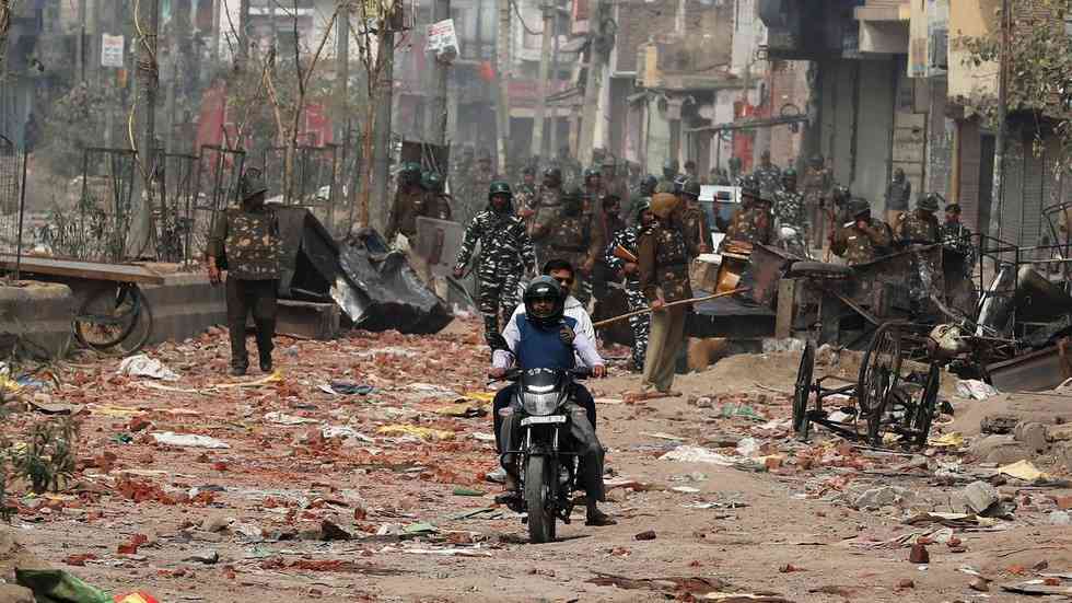 Men ride a motorcycle past security forces patrolling a street in a riot affected area after clashes erupted between people demonstrating for and against a new citizenship law in New Delhi, India, February 26, 2020